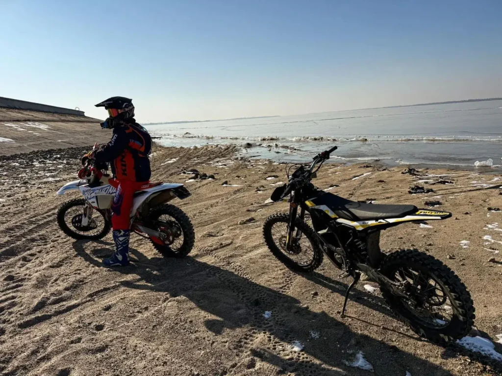 Surron Ultra Bee – elektryczny cross do wynajęcia z kamperem Elektryczny motocykl crossowy Surron Ultra Bee na piaszczystym brzegu – dodatkowa atrakcja do kampera
